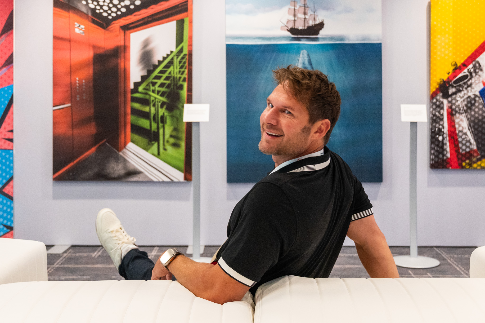 Neal Rosenblat seated in a lounge with colorful artwork behind him