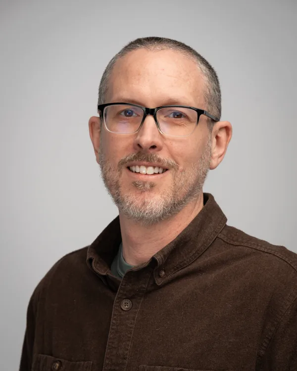 Studio headshot with glasses and a brown shirt