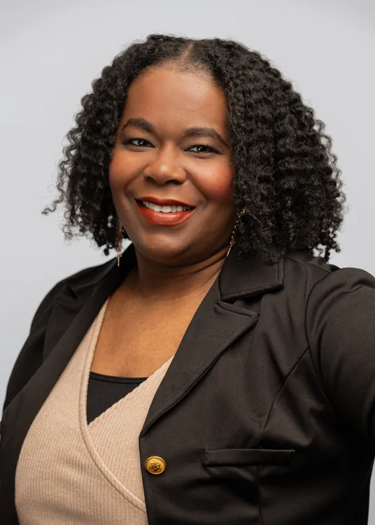 Studio headshot in a black blazer and gold buttons